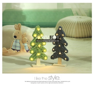 Detail of wool knitted Christmas tree decor with warm LED lights and wooden cross base