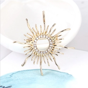 Detailed view of a golden sunburst brooch with crystal rhinestones on a ceramic dish