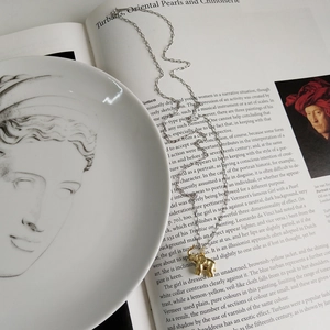 Artistic close-up of a gold elephant pendant necklace on a decorative white porcelain plate