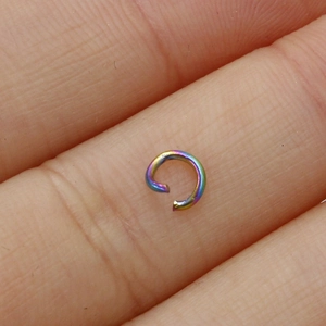 Close-up of small rainbow plated stainless steel open jump ring held on a fingertip