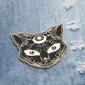 Detail of a black enamel cat head brooch with gold crescent moon and star on denim fabric