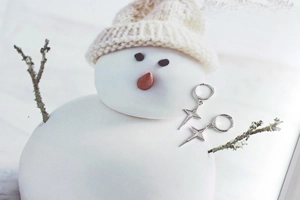 Close-up of silver star earrings on a snowman prop in a winter holiday setting