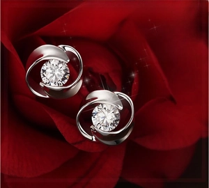 Macro shot of silver swirl stud earrings with round zircon on red rose petals