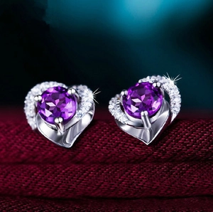Macro detail of heart-shaped silver earrings with purple center stone and white zircon