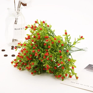 Close-up of artificial green leaves with red berries on a minimalist white desk