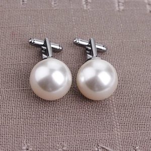 Close-up of pearl cufflinks with silver metal finish on textured brown fabric