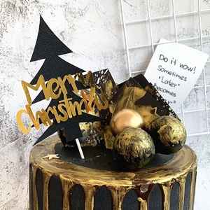 Détail du sapin noir et du cake topper Merry Christmas en acrylique doré posés sur un gâteau