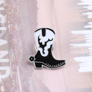 Detail shot of a black and white cowboy boot enamel pin with flame pattern and spur