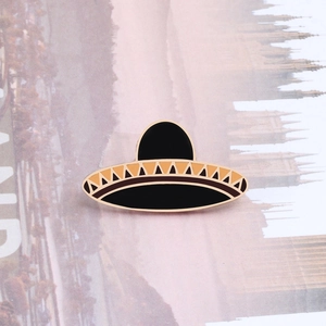 Detail of Mexican sombrero enamel pin with black and orange patterns and gold trim