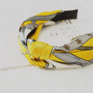 Detail view of knotted satin headband featuring yellow and grey patterns on silky fabric