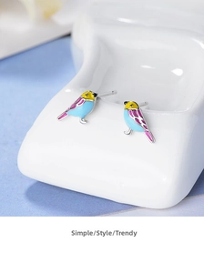 Macro shot of colorful enamel bird stud earrings on white ceramic base with soft light