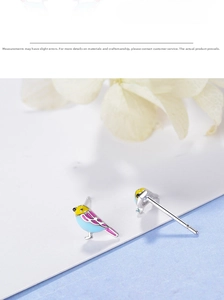 Macro shot of colorful enamel bird stud earrings with detailed yellow and blue hand-painted finish