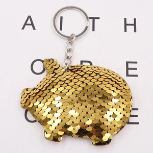 Detailed close-up of a golden sequin pig keychain with metallic ring on a white paper