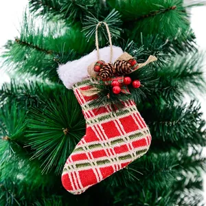 Knitted plaid Christmas stocking with pine cones hanging on a green tree branch