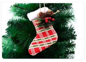 Close-up of a plaid Christmas stocking with pine cones and berries on a green branch