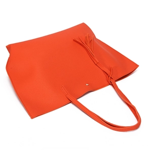 Detail of orange lychee textured leather tote bag with tassel charm on white background