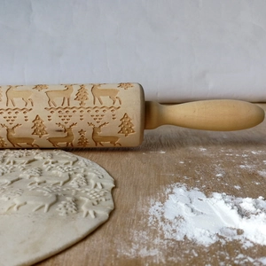 Detail of wooden rolling pin with reindeer and Christmas tree patterns on dough
