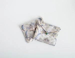 Detail of two white brocade jewelry pouches with blue wave embroidery and jade bead closure