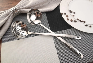 Close-up of stainless steel soup ladle and slotted spoon with leaf relief handle details
