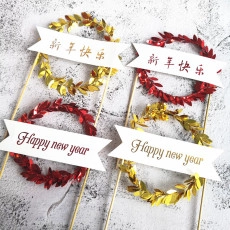 Close-up of gold and red New Year cake toppers with laurel wreaths on grey stone surface