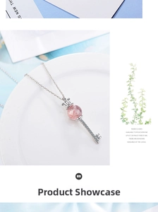 Detail shot of a silver crown key necklace with a pink strawberry crystal on a plate