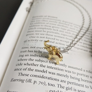 Close-up of a golden elephant pendant on a silver chain over a vintage book background