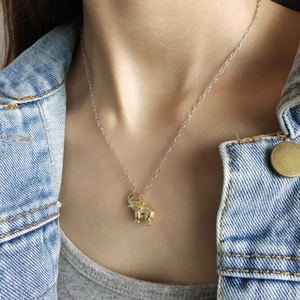 Close-up of a golden elephant pendant necklace worn over a denim jacket