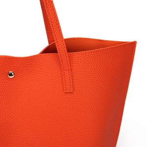 Detail view of orange lychee grain leather stitching and metal buckle on tote bag