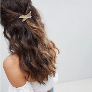 Detail of a golden leaf hair clip with crystals on wavy brown hair in a half-up style