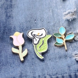 Detail showing colorful enamel pins with flower and leaf designs on denim fabric