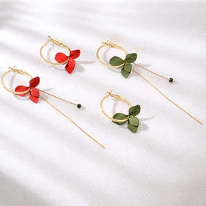 Détail de boucles d'oreilles asymétriques en pétales mats rouge et vert foncé avec pompons