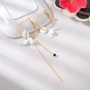 Détail de boucles d'oreilles asymétriques avec anneaux dorés et pétales de fleurs blanches