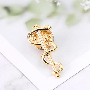 Macro view of gold-plated Caduceus medical brooch with detailed snake and staff engraving