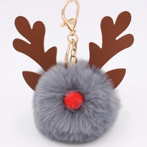 Close-up of a Christmas reindeer plush pompom keychain with golden metal ring and dark gray fur