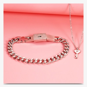 Detailed shot of silver steel heart lock bracelet and key necklace set on pink background