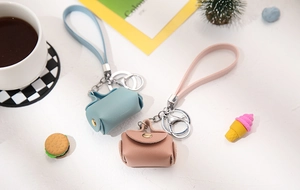 Miniature PU leather keychain bags in blue and pink on a styled desktop setting