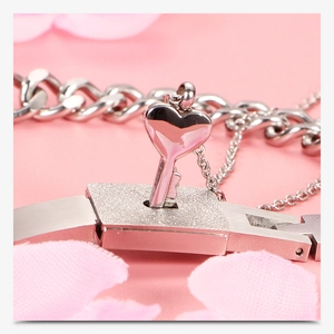 Macro shot of silver heart lock and key bracelet set against soft pink floral background