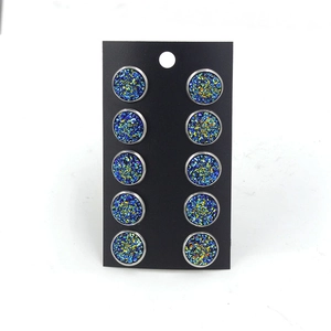 Détail de cinq paires de clous en acier titane argenté 12mm avec paillettes bleu-vert