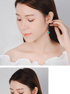 Detail shot of long silver star earrings with green stones worn by a model