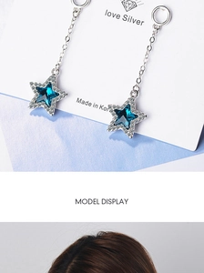 Macro view of long silver star drop earrings with blue crystals on card and model display