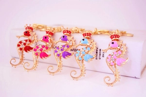 Close-up of five colorful rhinestone seahorse keychains with crowns on a book