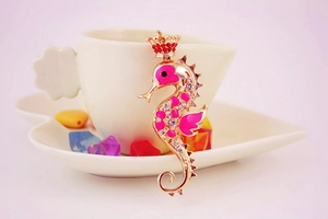 Detail of pink enamel seahorse keychain with crystal rhinestones on a white saucer