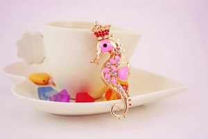 Detail of pink enamel seahorse keychain with crown and crystals on a beige heart saucer