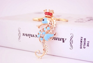 Macro detail of golden seahorse keychain with blue enamel, crystals, and red crown