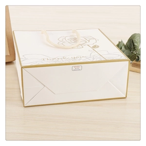 Elegant white gift bag with gold rose pattern and Thank You text on wooden background