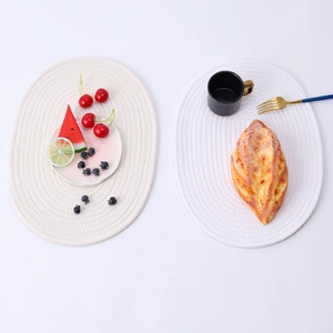 Detail of two white oval woven cotton rope placemats with concentric texture