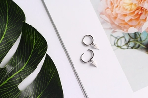Minimalist S925 silver hoop earrings with geometric cone pendants on a floral magazine