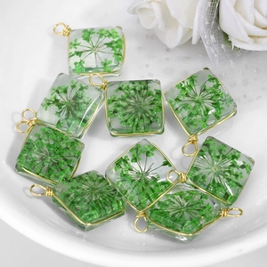 Square clear resin pendants with green dried flowers and gold metal frame on white plate