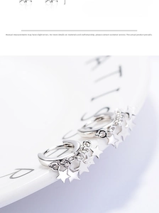 Macro shot of silver star hoop earrings featuring small polished star charms on white ceramic