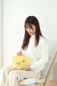 Detail of transparent PVC makeup bag with yellow polka dots held by a model in a bright room